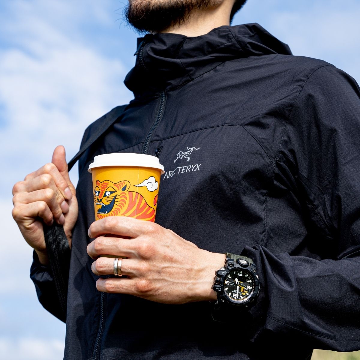 A person holding a specialty coffee cup while wearing an Arc'teryx jacket, representing the union of specialty coffee and nature.